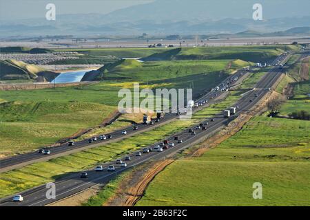 Interstate Highway I5 im zentralen Tal des CA-Verkehrs, California Aqueduct Water im Hintergrund und weiße Bäume von Almond Bloom in Richtung Norden links Stockfoto