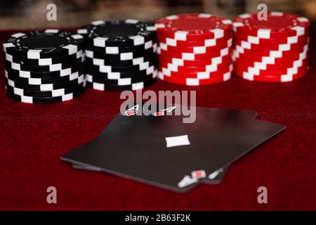 Ein Paar Asse, Herzen und Diamanten, mit einem einzigartigen schwarzen Kartendeck mit roten und schwarzen Ton-Pokerchips in einem symetrischen Muster, das auf einem maro gesetzt ist Stockfoto