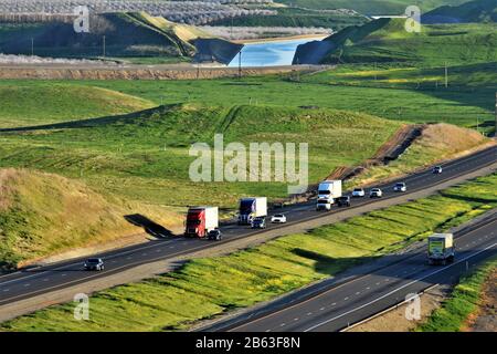 Interstate Highway I5 im zentralen Tal des CA-Verkehrs, California Aqueduct Water im Hintergrund und weiße Bäume von Almond Bloom in Richtung Norden links Stockfoto