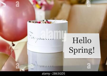 Text Hello Spring auf weißer Karte mit Blumenkasten. Weißer Hut runder Kasten mit rosa Rosen Blumen und Text Für Sie. Festliche Ballons in Pink und Gold. Stockfoto