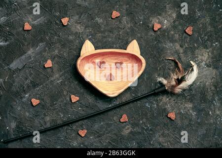 Holzplatte in Kopfkatze mit Lieblingssnacks für Haustiere und Spielzeug, dunkler Hintergrund. Draufsicht. Konzeptpflege, Haustiere füttern Stockfoto