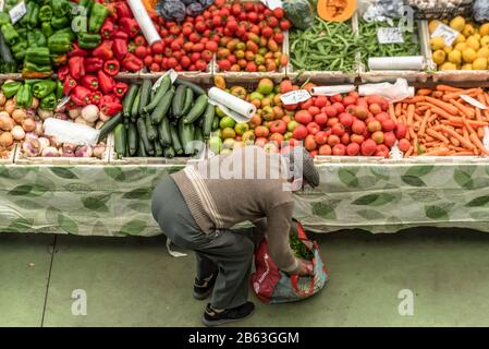 Cascais, Portugal - 14. August 2019: Ein alter Mann, der Hut trägt und sich verbiegt, um frisches Gemüse zu verpacken, das an einem Obst- und Gemüsestall bei Cas gekauft wurde Stockfoto