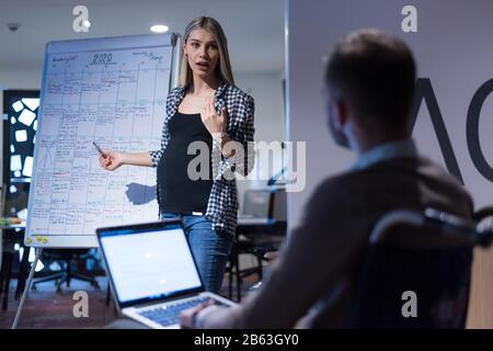 Behinderter junger Mann mit seinen Kollegen, die im Büro arbeiten. Behinderter Geschäftsmann im Rollstuhl und seine Kollegen listetning Präsentation der Thei Stockfoto