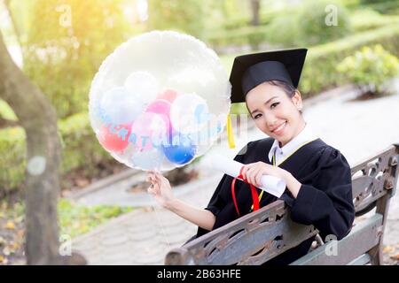 Porträt der glückliche junge Frauen bei den Hochschulabsolventen in den akademischen Kleidung und Square akademischen Cap halten Wort Zitate von CONGRATS Grad auf Ballon nach Einberufung c Stockfoto