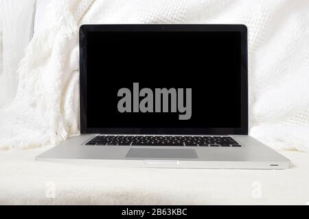 Moderner Laptop, der sich auf einer weichen weißen Decke auf der Couch entspannen kann. Verfügt über einen Beschneidungspfad im Bildschirm, um das Hinzufügen eines eigenen Bildes zum Bildschirm zu erleichtern. Stockfoto
