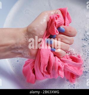 Weibliche Hand mit blau Nägel Waschen ein rosa T-Shirt in einem Becken Stockfoto