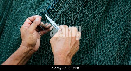 Hand des Fischers repariert ein Netz mit einem Messer Stockfoto