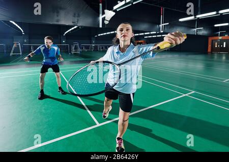 Konzentriertes Paar, das in der Mannschaft im Gymnasium Badminton spielt Stockfoto