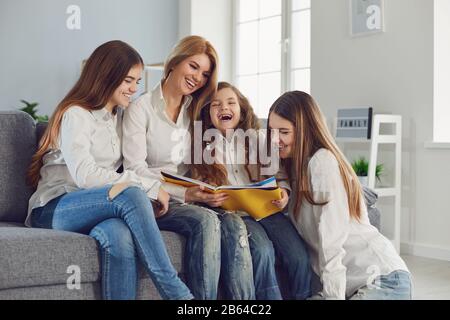 Mutter mit Kindern liest ein Buch, während sie auf einem Sofa in einem Zimmer sitzt. Stockfoto