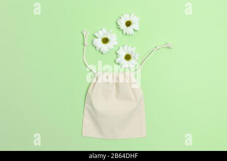 Weiße Kamillenblumen und Leinwandsack auf grünem Hintergrund. Kunststofffreies Konzept. Stockfoto