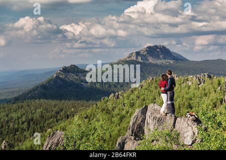 Rückansicht, Paar Wanderer, die in die Ferne blicken, steht auf dem Gipfel des Bergfelses. Hintergrund ist der Gebirgszug und der blaue Himmel. Stockfoto