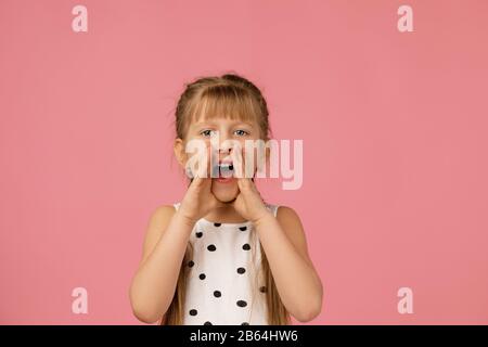 Kind ruft jemanden an. Süßes kleines Mädchen schreit und hält ihre Hand in der Nähe ihres Mundes auf Studio rosa Hintergrund Stockfoto