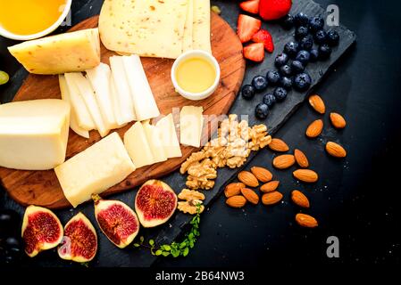 Käseplatte. Sortiment von Käse mit Walnüssen, Mandeln, Trauben, Feigen und Erdbeeren, Heidelbeeren und Honig Stockfoto