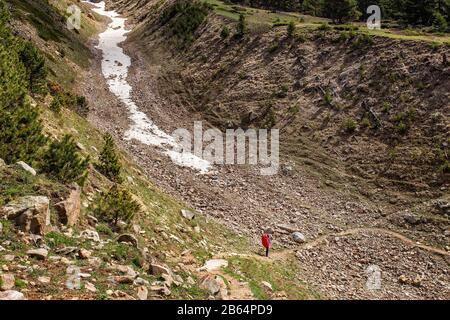 Man Backpacker wandern in einem tiefen Schluchtschluchtschlucht des trockenen Flussbetts zwischen riesigen roten Felsklippen und Kaukasusbergen Stockfoto