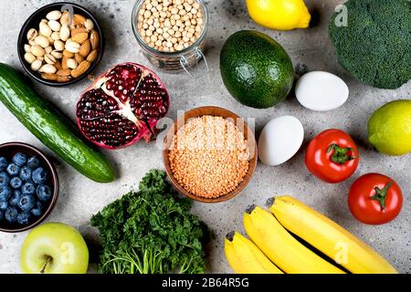 Gesundes veganes Ernährungskonzept. Grünes Gemüse, Tomaten, Nüsse, Bohnen und Obst auf leichtem Betontisch. Flache Lage, Draufsicht Stockfoto