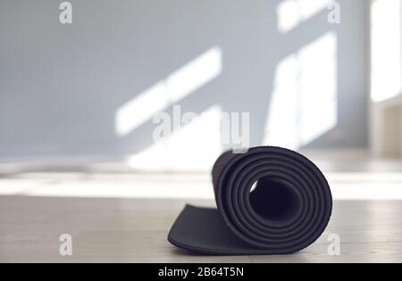 Schwarze Yogamatte auf dem Boden eines hellen, sonnigen Studios. Stockfoto