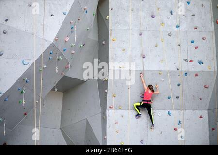 Schöne junge Frau beginnt, große künstliche Wand zu erklimmen Stockfoto