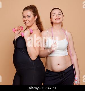 Übergewichtige Mädchen in Fitnessklassen, posieren mit Hanteln und Springseil Stockfoto