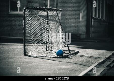 Fußball kleine Tore mit einem zerrissenen Netz, in dem ein gepunktter blauer Fußball liegt. Die Tore sind vergessen und verlassen und niemand ist da. Stockfoto