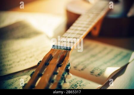 Eine alte, von hellem Sonnenlicht beleuchtete Akustikgitarre liegt auf dem Tisch in der Nähe der Noten aus den Melodien. Stockfoto