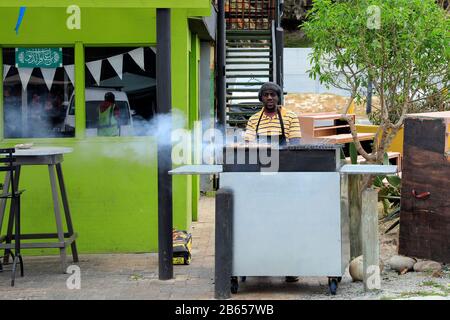 Mann grillen im Restaurant im Hafen von Hout Bay in der Nähe von Kapstadt, Südafrika. Stockfoto