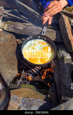 Eier, die in einer Gusseisenpfanne auf dem Campingfeuer gebraten werden Stockfoto