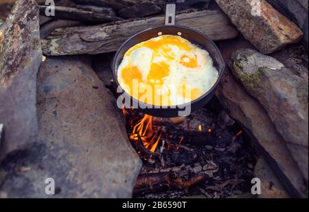 Eier, die in einer Gusseisenpfanne auf dem Campingfeuer gebraten werden Stockfoto