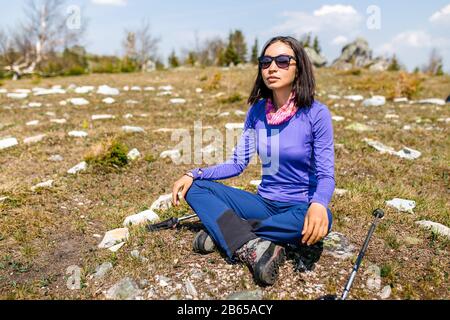 Eine junge Frau, die auf einem Felsvorsprung in den Bergen sitzt Stockfoto