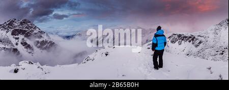 Der Mann in der Jacke steht und genießt den Blick auf die Schneeberge Stockfoto