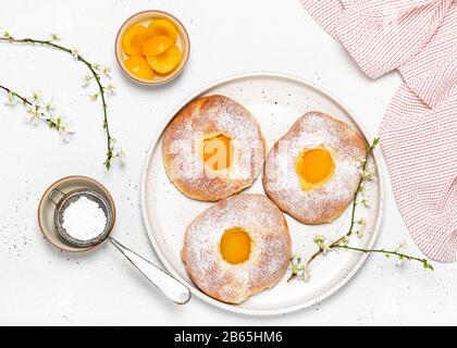 Hausgemachtes Backen. Easter Teigbrötchen mit Aprikosen und Puderzucker auf einem weißen Gaumen zum Frühstück. Draufsicht. Stockfoto
