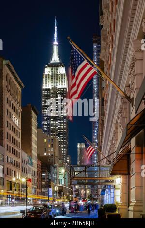 New York City/USA - OCT 18 2018: Straßenansicht des Empire State Building in der Dämmerung mit Verkehr, Menschen und Flagge in New York City USA Stockfoto