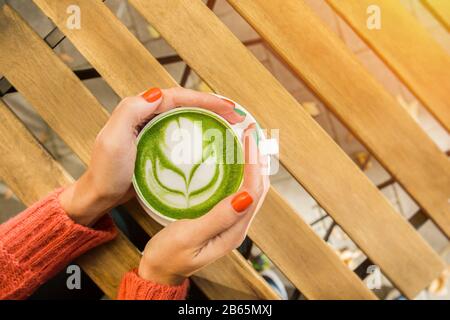 Weibliche Hände halten Tassen matchgrünen Tees auf rustikalem Holztisch. Trendy powered Tea. Stockfoto