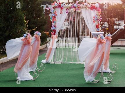 Schöner weißer Bogen mit Blumenschmuck für die Hochzeitsfeier auf grünem Grund mit Bäumen Stockfoto