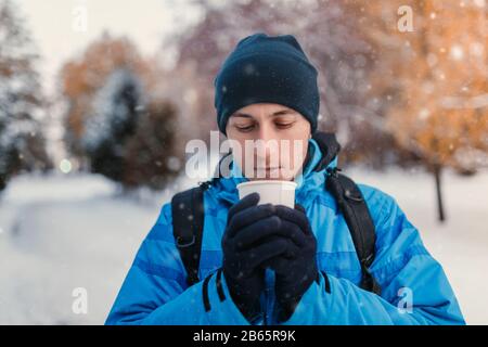 Porträt eines Mannes, der eine leuchtend blaue sportliche Winterjacke trägt und Heißgetränk in Einweg-Papierbecher hält, Außenaufnahme Stockfoto