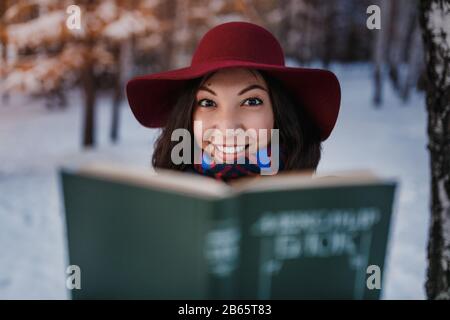 Schöne Mädchen lächeln und verbirgt ihr Gesicht hinter einem Buch. Außenporträt Stockfoto