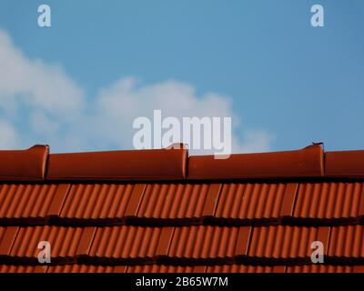 Modernes hellbraun-rotes Lehmziegel schiefergedecktes Wohndach und Lehm. Klarer blauer Himmel und weiße Wolken. Baukonzept. Moderne Dachdeckmaterialien Stockfoto