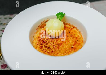 Kugeln aus cremefarbenem Brulee-Eis mit Zitronenkugelsorbet und Minzsprig auf weißem Plattenhintergrund Stockfoto