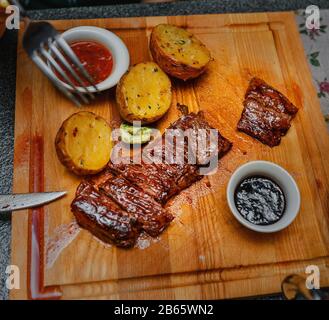 Roastbeef mit Kartoffeln und Tkemali-Sauce auf einem Holzbrett Stockfoto