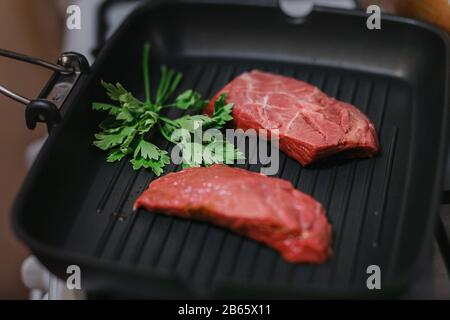 Zwei köstliche Stücke rohes Rindfleisch mit Petersilie in einem Pfannengrill Stockfoto