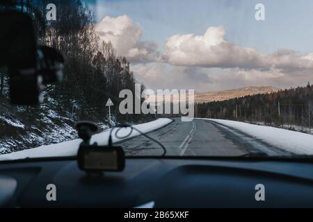 Blick vom Auto im Inneren mit einem Teil des Torpedos auf Gefahr und schöne gebogene Eisasphalt-Straße mit schneebedeckten Bergen. Film-Vintage-Effekt hinzugefügt. Stockfoto