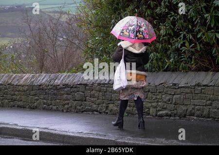 Eine junge Frau, die im Regen einen Regenschirm trägt, läuft auf der Spring Bank in New Mills, Derbyshire. Stockfoto