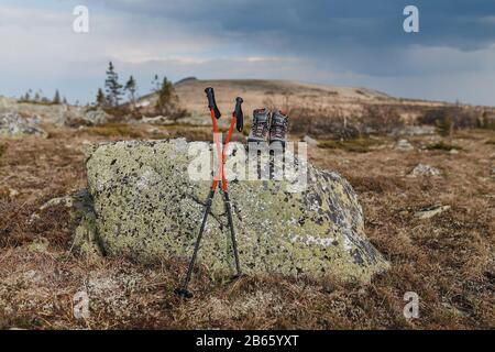 Wanderstiefel mit Trekkkingstöcken auf dem Gras im Hintergrund der uralischen Gebirgskette im Frühling Stockfoto