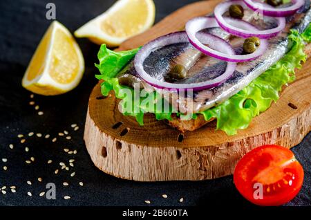 Ein norwegischer junger Heringsschmorrebrod mit Salat, blauer Zwiebel, Zitrone und Sesam liegt auf einer Holzplatte. Nahaufnahme Stockfoto