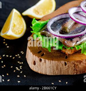 Ein norwegischer junger Heringsschmorrebrod mit Salat, blauer Zwiebel, Zitrone und Sesam liegt auf einer Holzplatte. Nahaufnahme Stockfoto