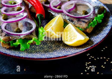 Ein norwegischer junger Heringsschmorrebrod mit Salat, blauer Zwiebel, Zitrone und Sesam liegt auf einer Holzplatte. Nahaufnahme Stockfoto