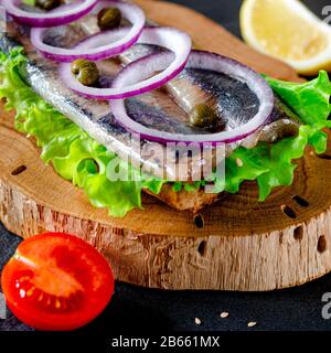 Ein norwegischer junger Heringsschmorrebrod mit Salat, blauer Zwiebel, Zitrone und Sesam liegt auf einer Holzplatte. Nahaufnahme Stockfoto