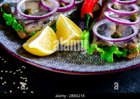 Ein norwegischer junger Heringsschmorrebrod mit Salat, blauer Zwiebel, Zitrone und Sesam liegt auf einer Holzplatte. Nahaufnahme Stockfoto