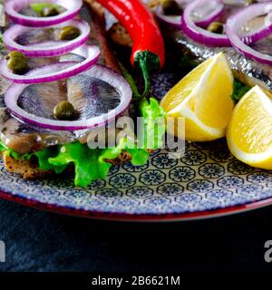 Ein norwegischer junger Heringsschmorrebrod mit Salat, blauer Zwiebel, Zitrone und Sesam liegt auf einer Holzplatte. Nahaufnahme Stockfoto