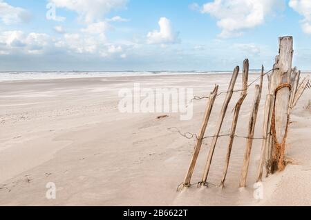 Strand und Nordsee an einem stürmischen, aber sonnigen Tag auf der Maaslvakte bei Rotterdam in den Niederlanden. Die Überreste eines Holzzauns sind in der Vorhand Stockfoto