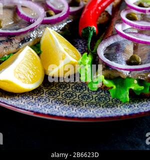 Ein norwegischer junger Heringsschmorrebrod mit Salat, blauer Zwiebel, Zitrone und Sesam liegt auf einer Holzplatte. Nahaufnahme Stockfoto